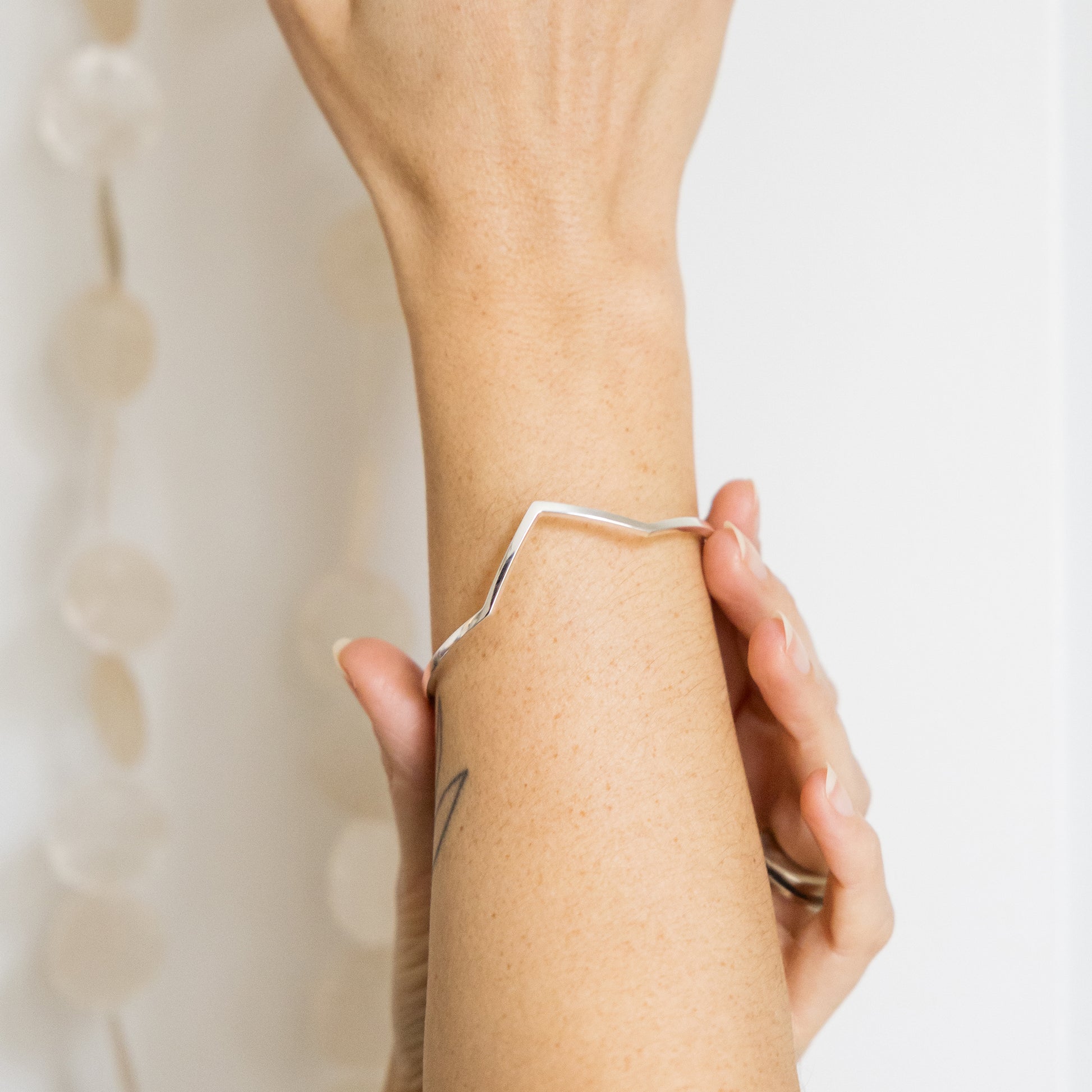 Person wearing a delicate silver bracelet on a light background