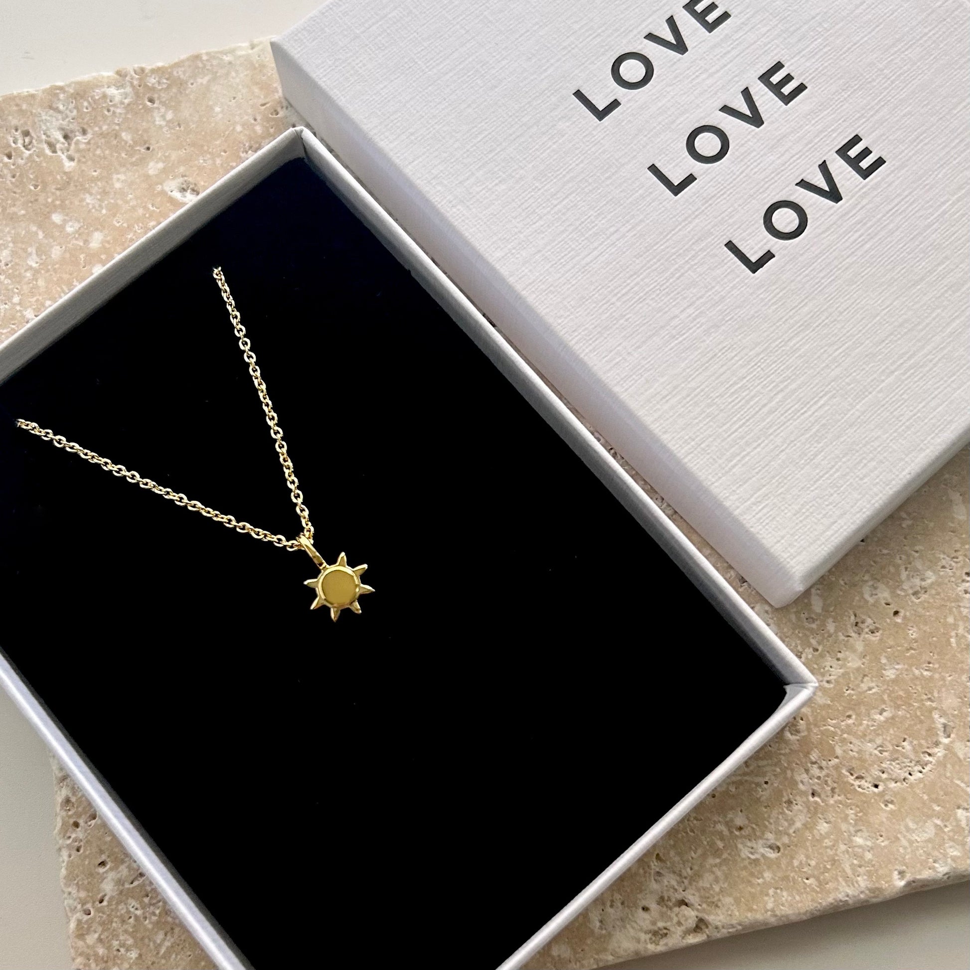 Gold necklace with sun pendant in a box labeled 'LOVE'.