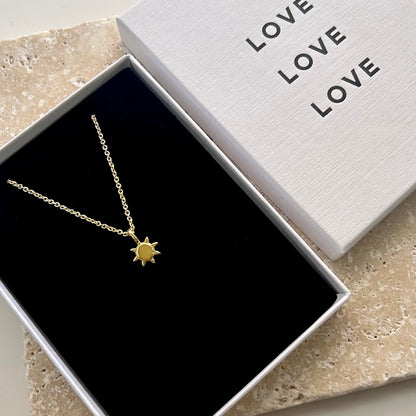 Gold necklace with sun pendant in a box labeled 'LOVE'.