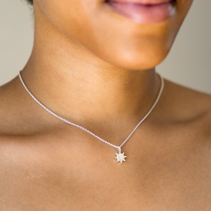 Silver necklace with a sunshine pendant worn by a person