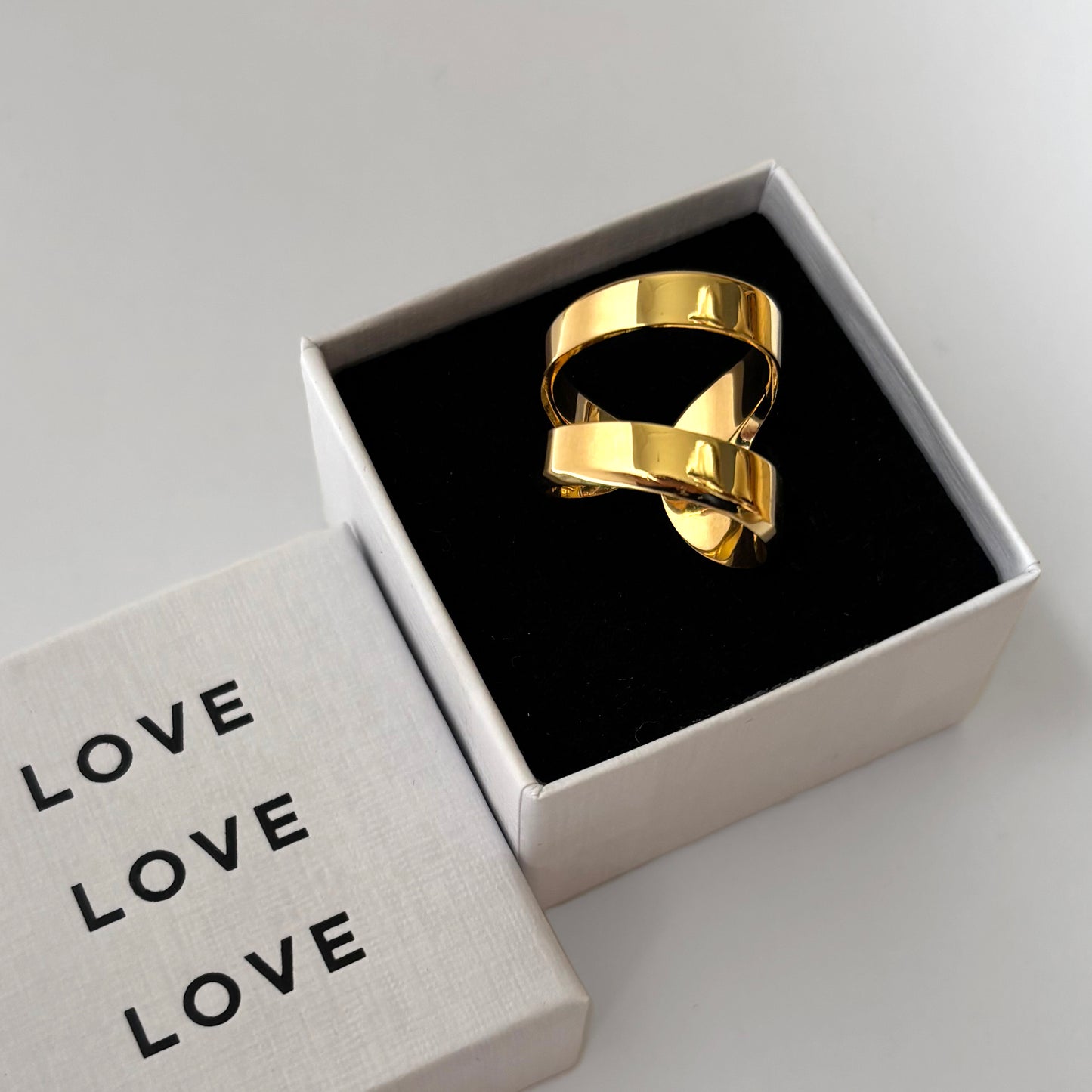 Gold ring in a box with 'LOVE' text on a light gray background
