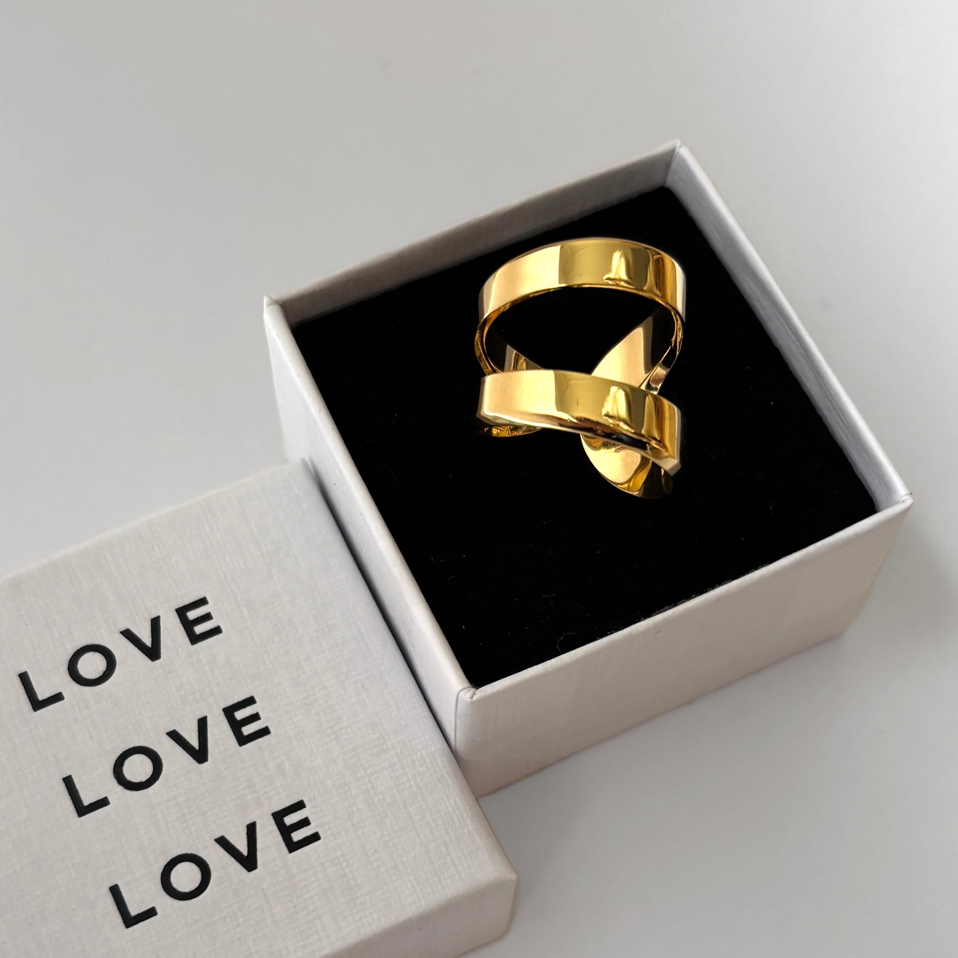 Gold ring in a box with 'LOVE' text on a light gray background