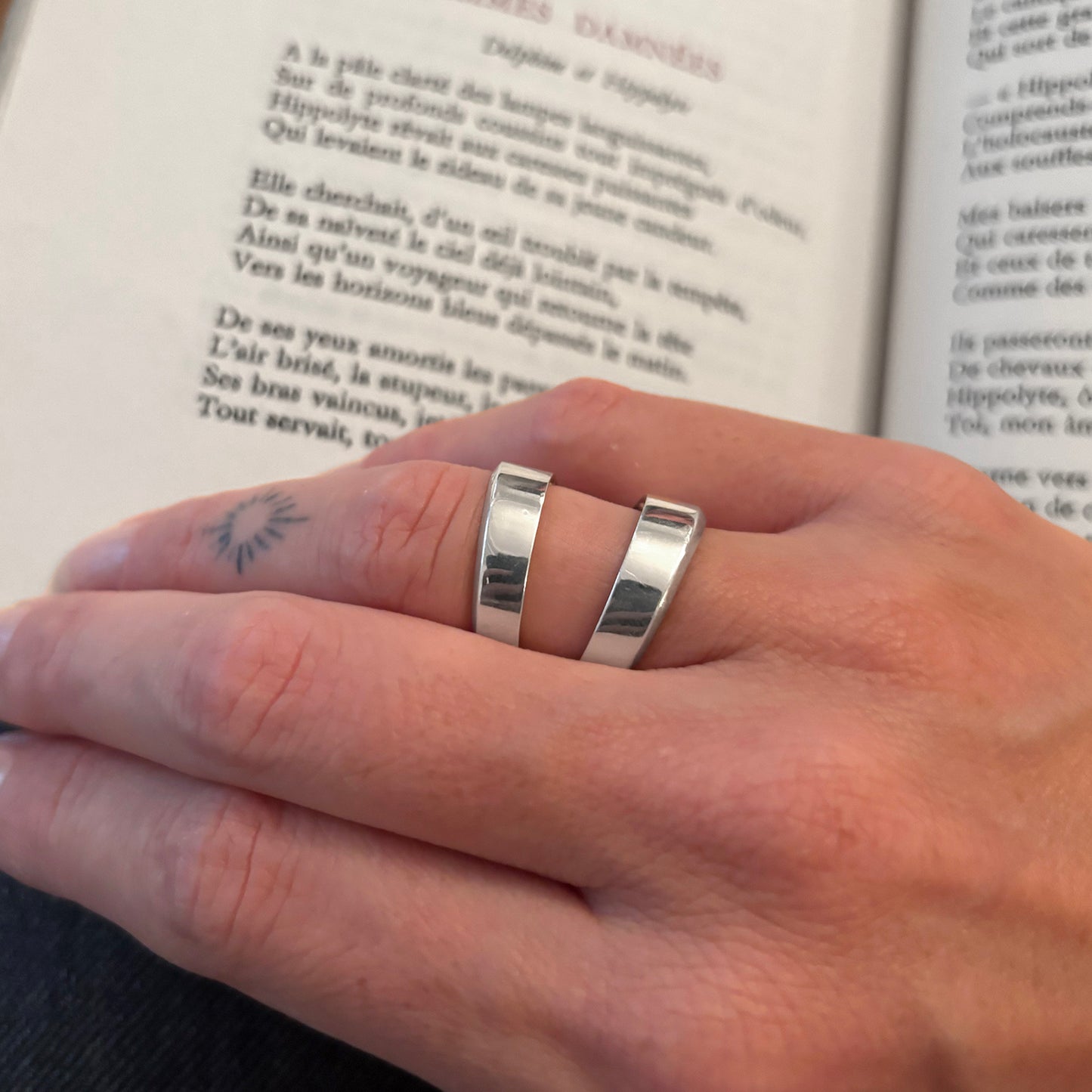 Close-up of a hand wearing a silver ring with an open book in the background.