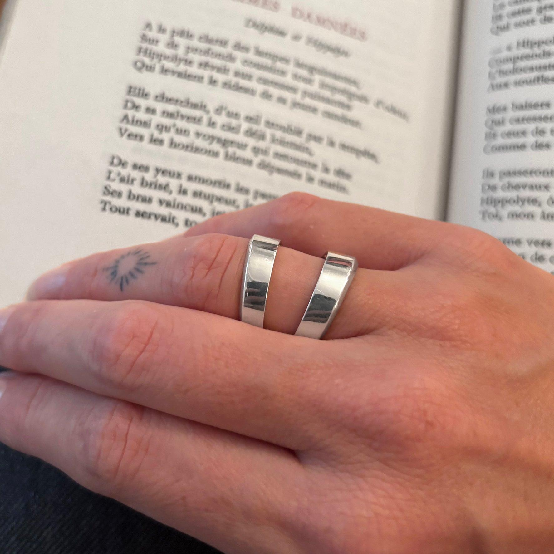 Close-up of a hand wearing a silver ring with an open book in the background.