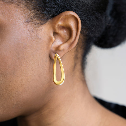Gold teardrop earring jewelry worn by a person with a neutral background