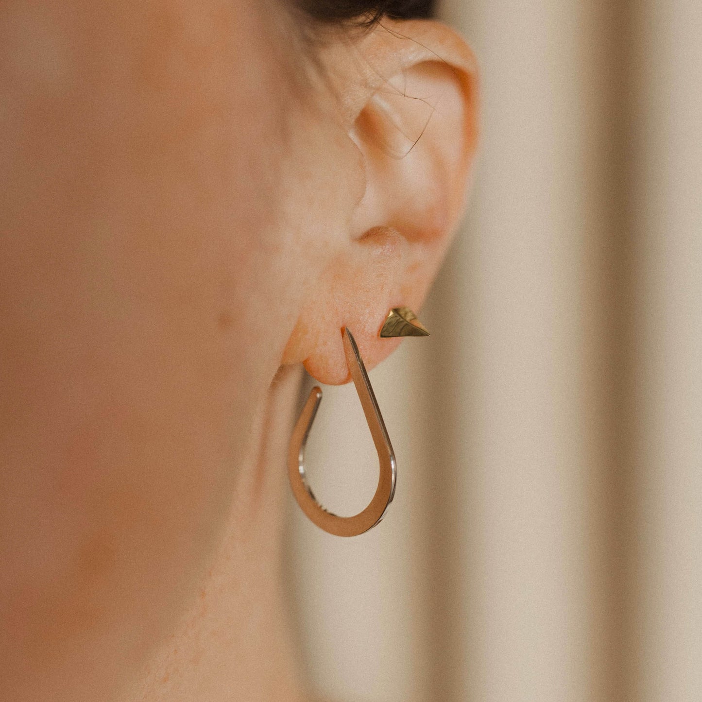 Close up of a person wearing a teardrop-shaped earring and a pointed stud earring.