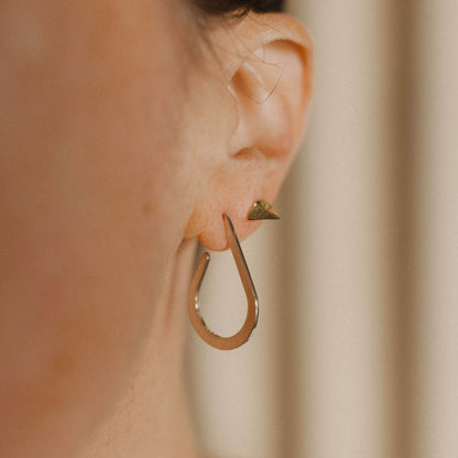Close up of a person wearing a teardrop-shaped earring and a pointed stud earring.