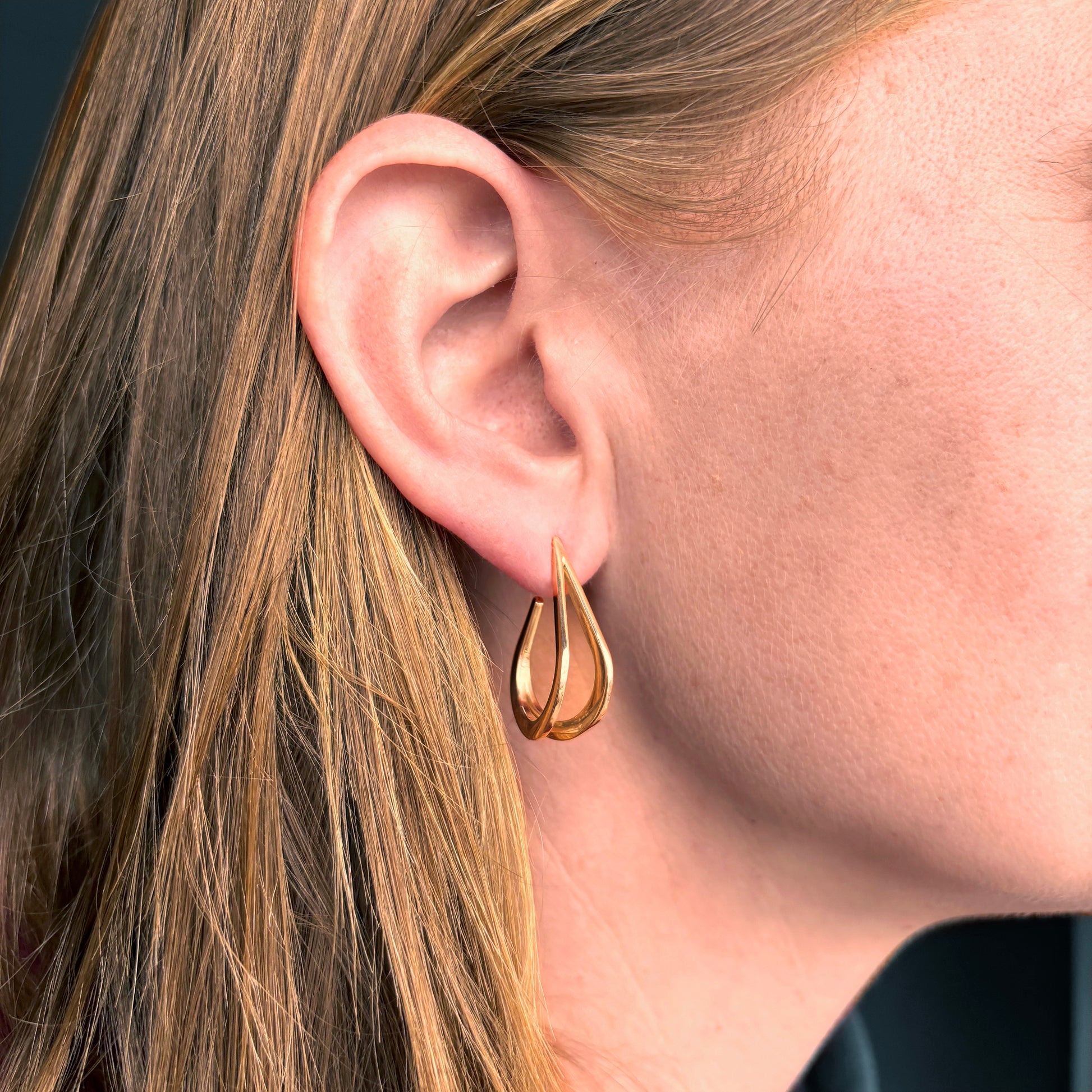 Gold teardrop earring worn by a person with blonde hair.