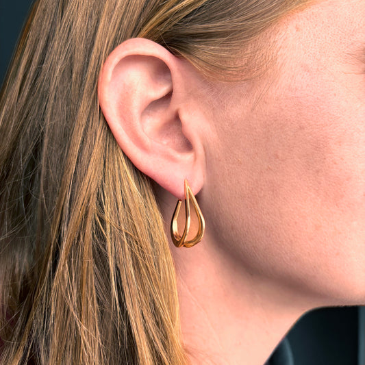 Gold teardrop earring worn by a person with blonde hair.