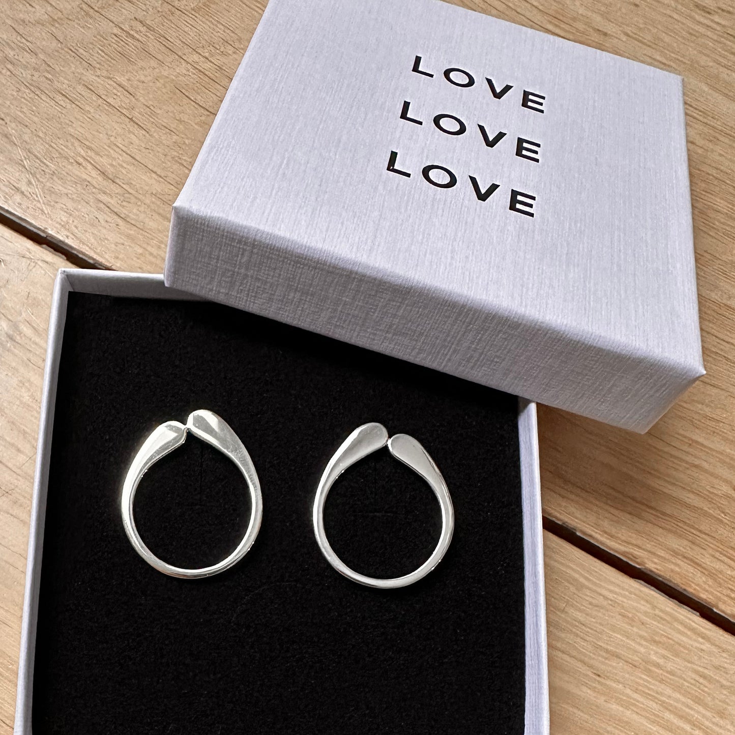 Silver hoop earrings in a box with 'LOVE' text on a wooden surface