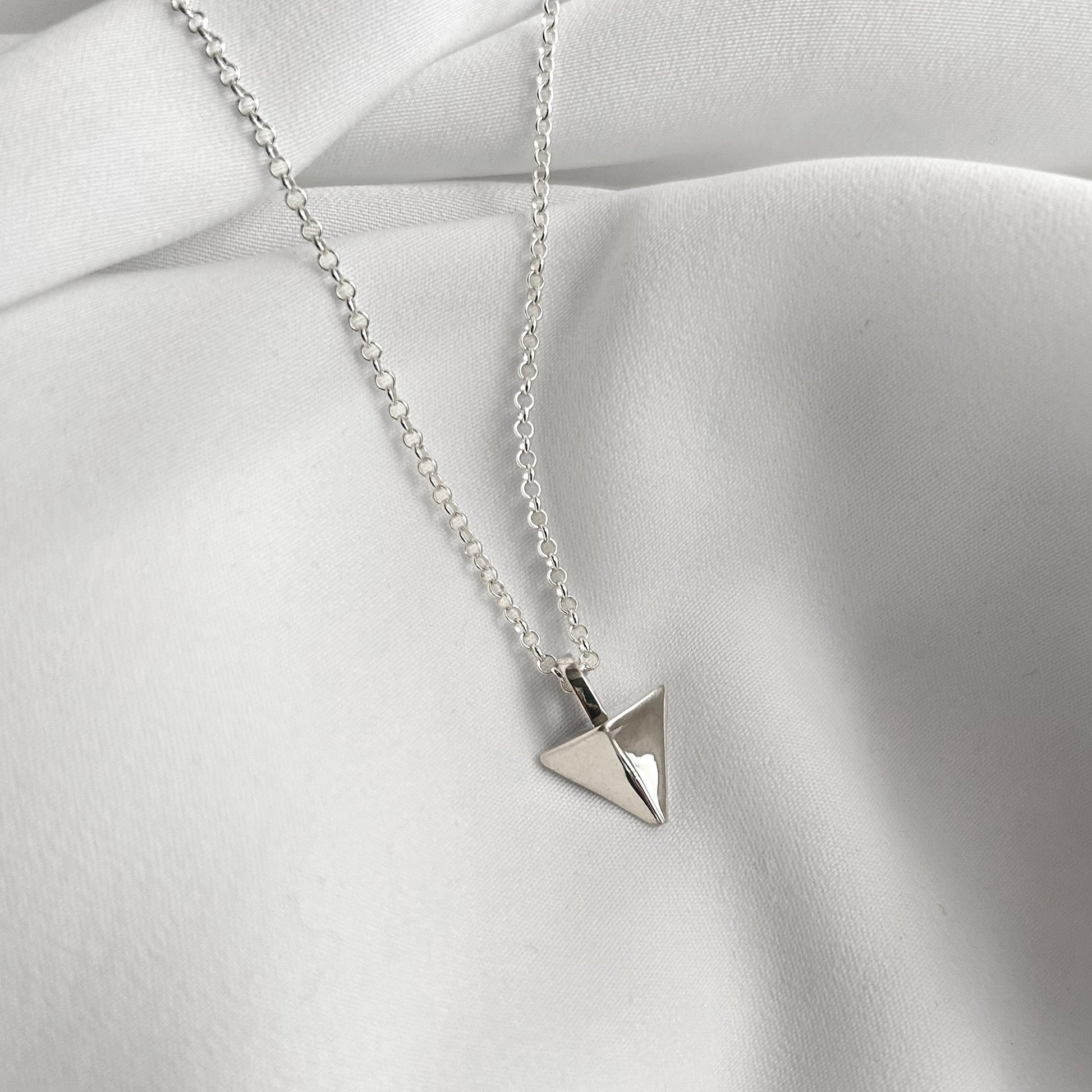 Silver triangle pendant necklace on a light fabric background
