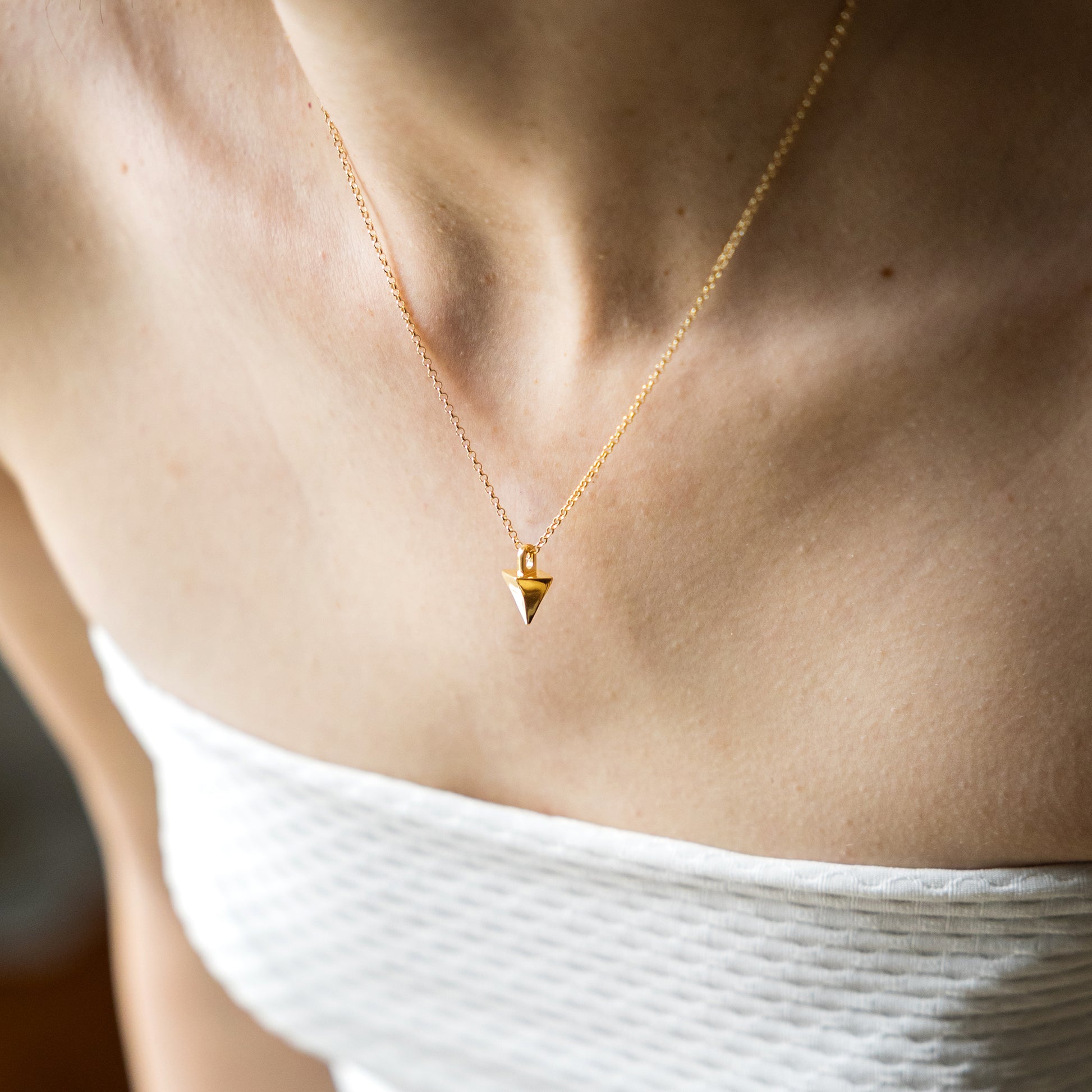 Gold necklace with a triangular pendant on a person wearing a white top.