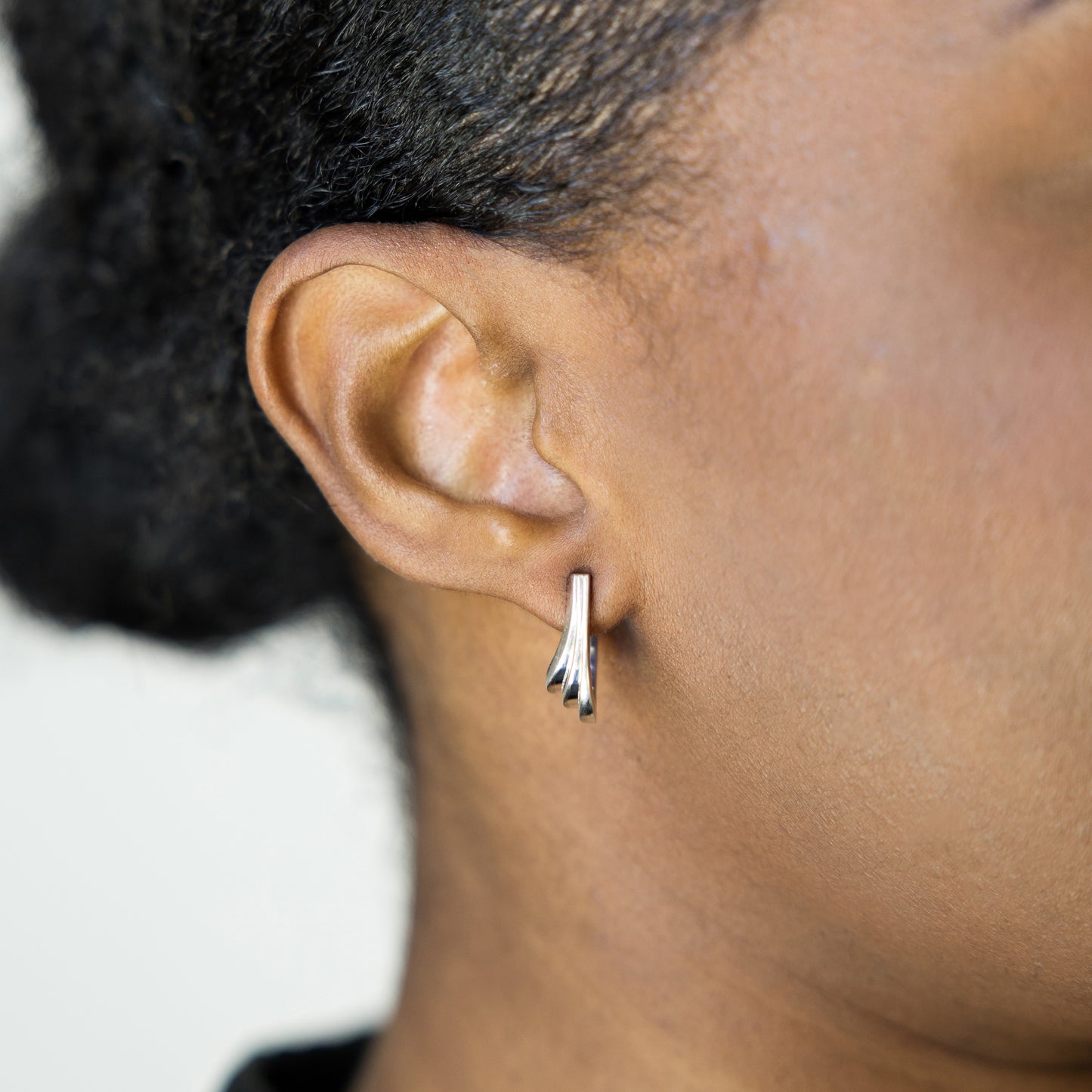 Close-up of an ear wearing a silver earring with a blurred background