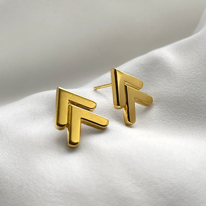 Gold geometric earrings on a white fabric background