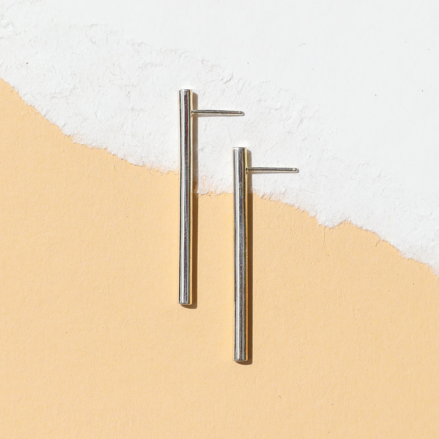 A pair of silver-colored linear drop line earrings with a tubular design, displayed against a white background.
