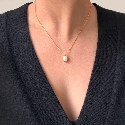 A close up of a person wearing a pearl pendant necklace with a gold chain.