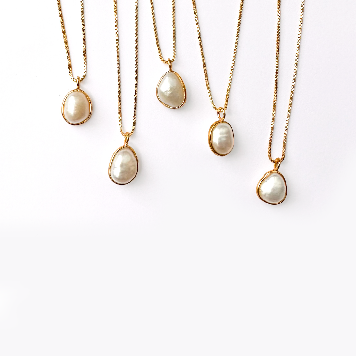Five gold necklaces with pearl pendants hanging against a white background