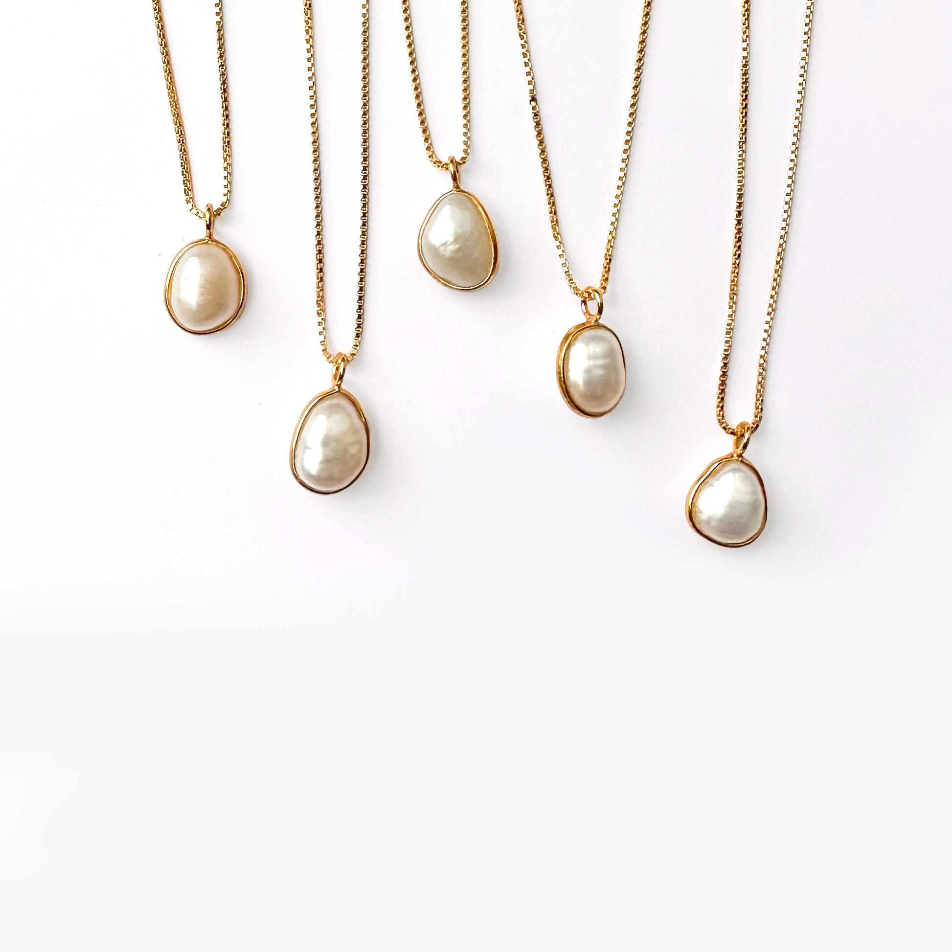 Five gold necklaces with pearl pendants hanging against a white background