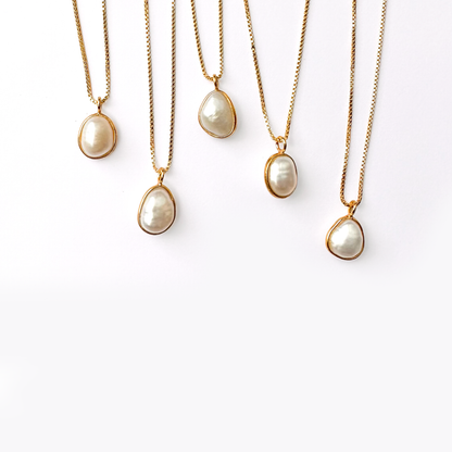 Five gold necklaces with pearl pendants hanging against a white background