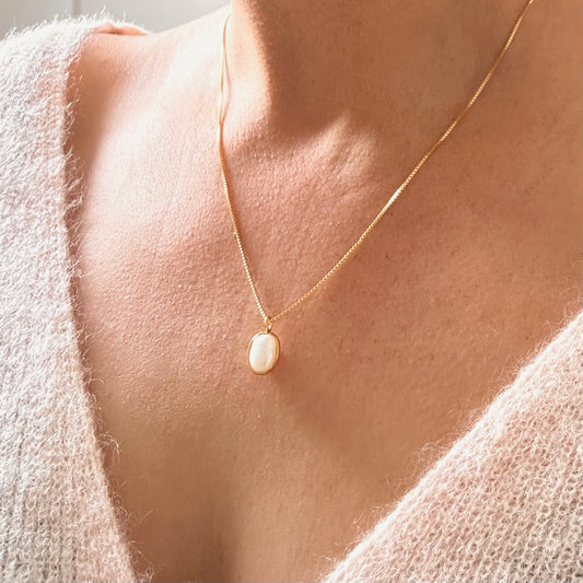 A close up of a person wearing a gold necklace with a pearl pendant.