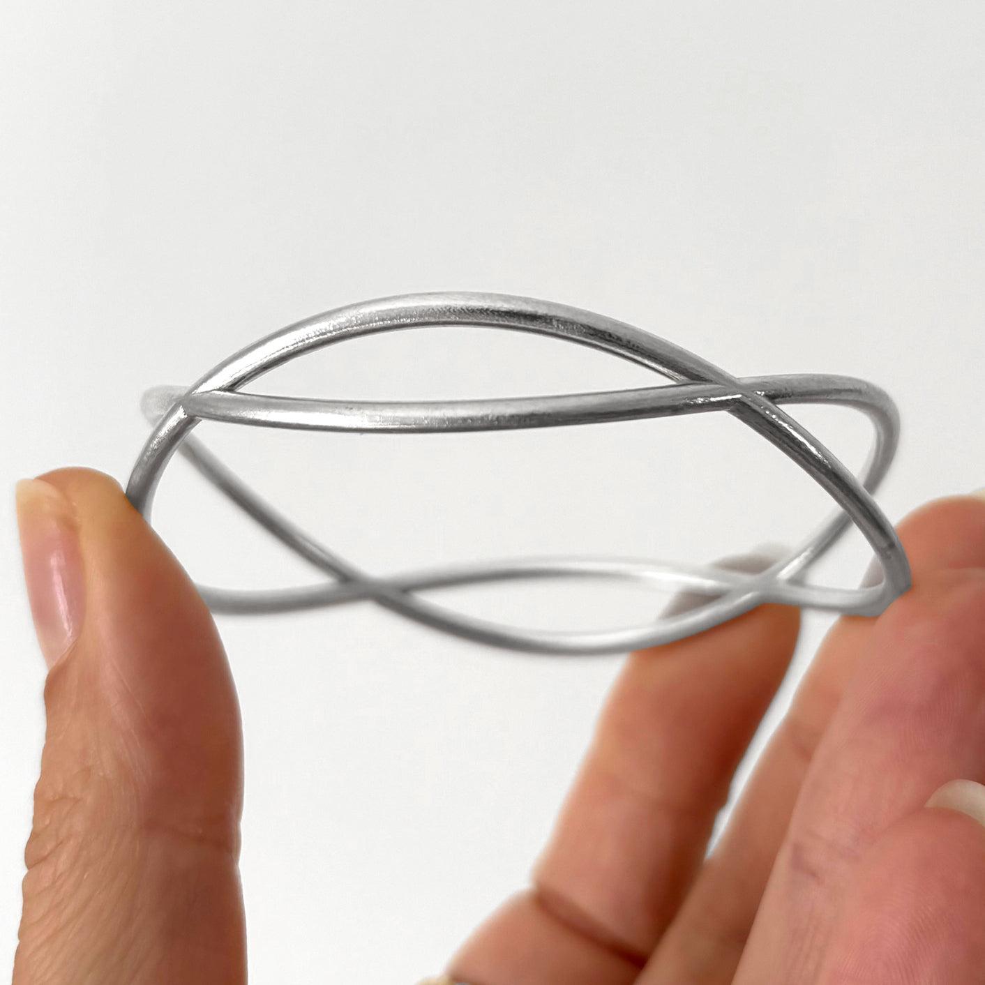 Hand holding jewelry, a silver wave bracelet against a white background