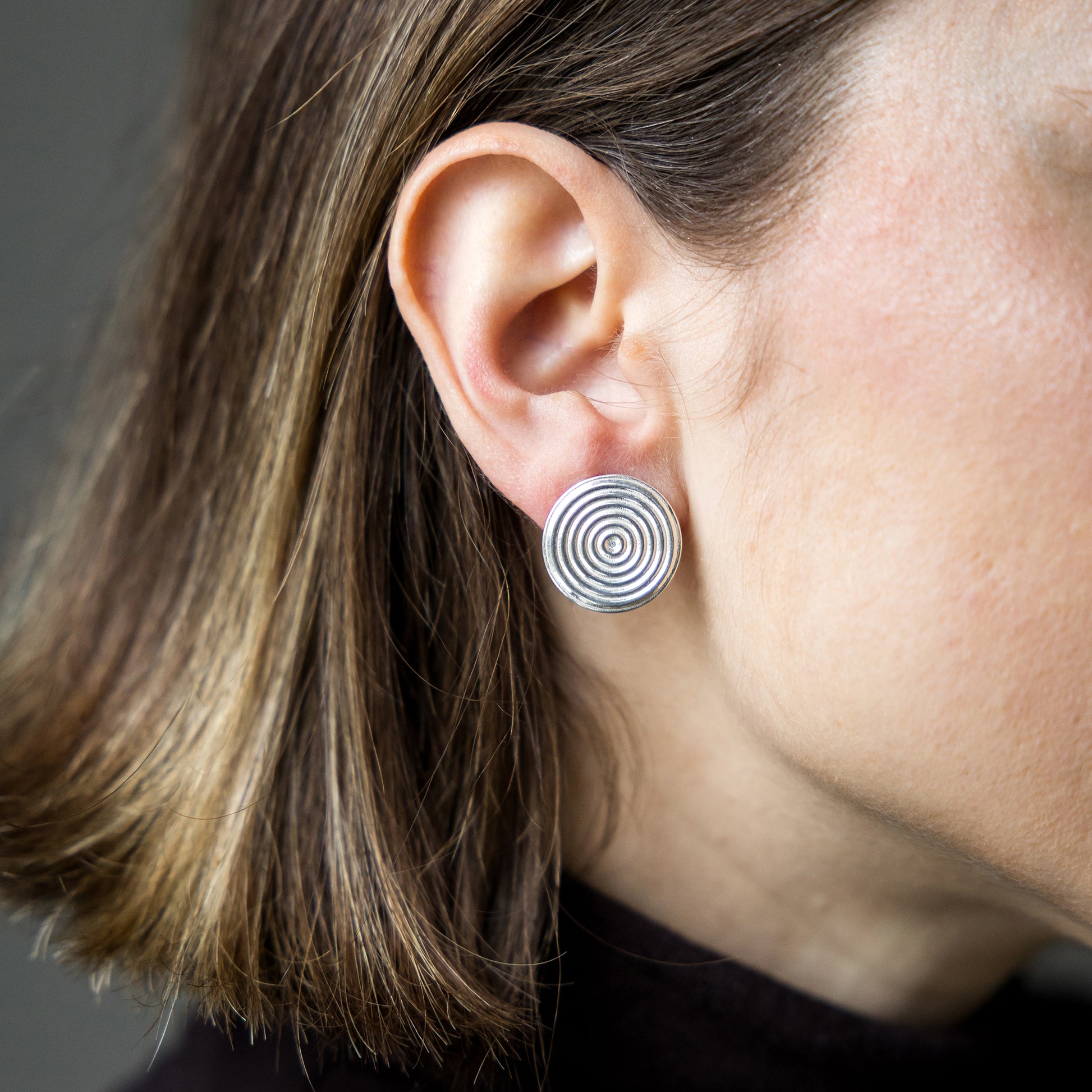 Close-up of an ear wearing a silver spiral earring against a neutral background