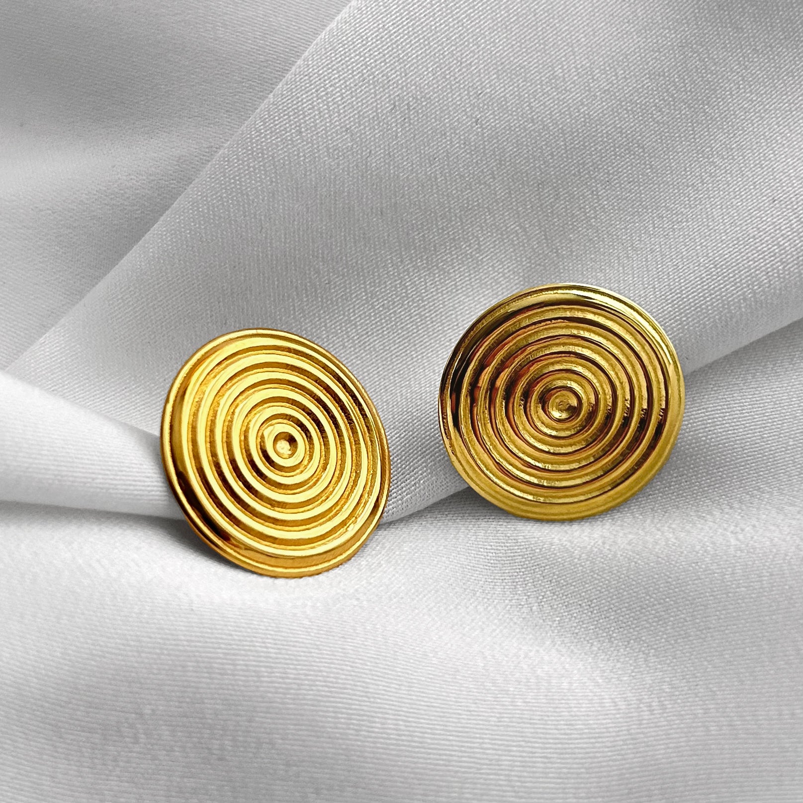 Pair of gold spiral earrings on a light gray fabric background