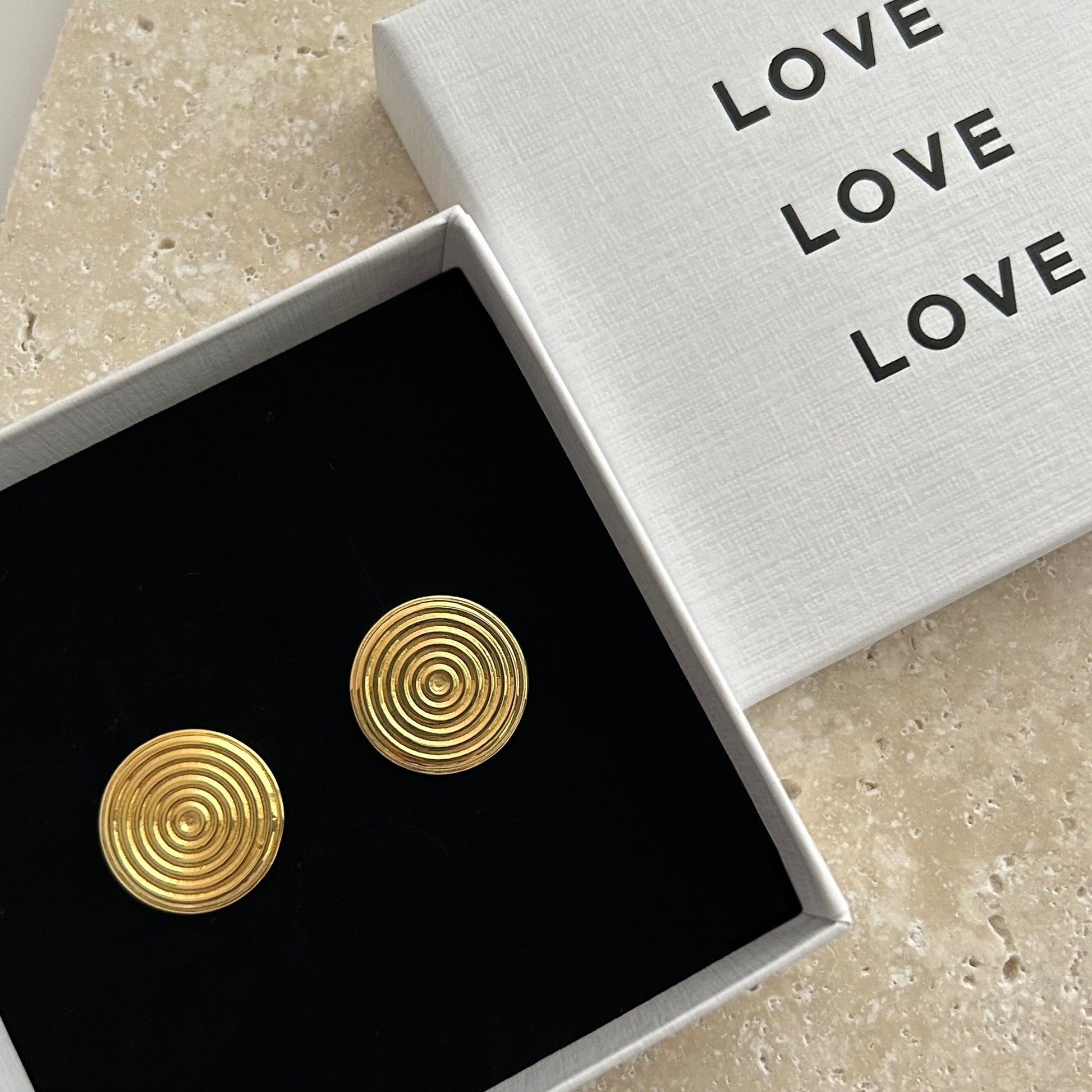 Gold circular earrings in a box with 'LOVE' text on a beige surface