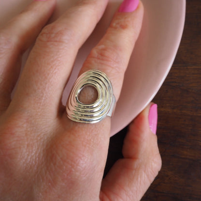 Silver ring with a unique design worn on a finger with pink nail polish.