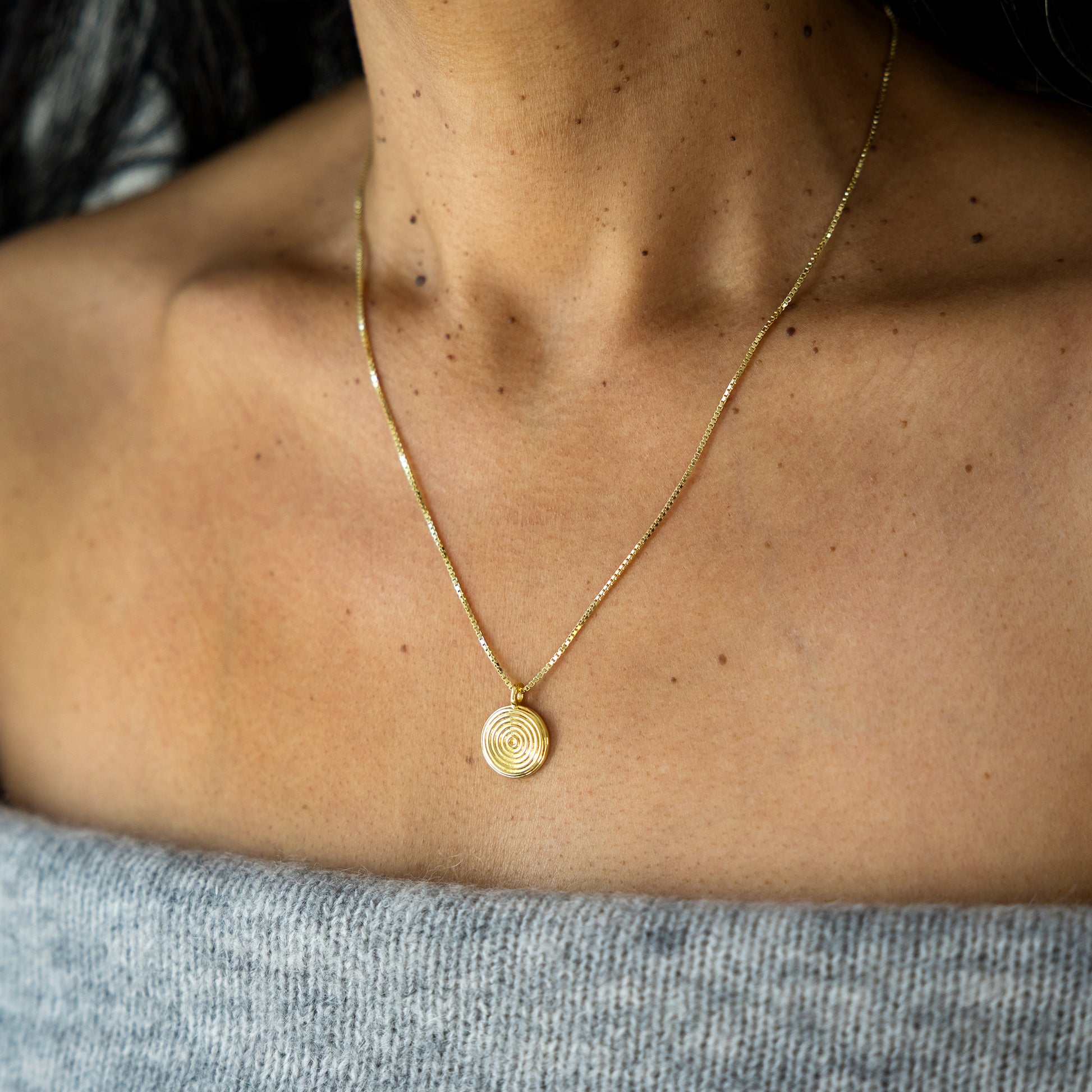 Gold necklace with a circular pendant on a person's neck