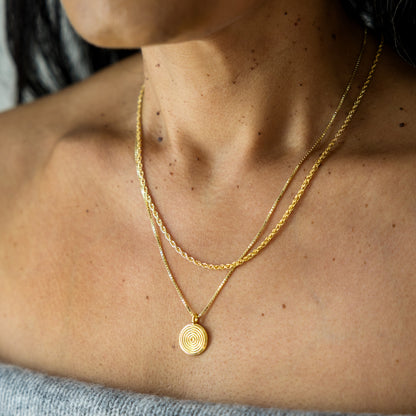 Close-up of a person wearing a gold necklace with a circular pendant.