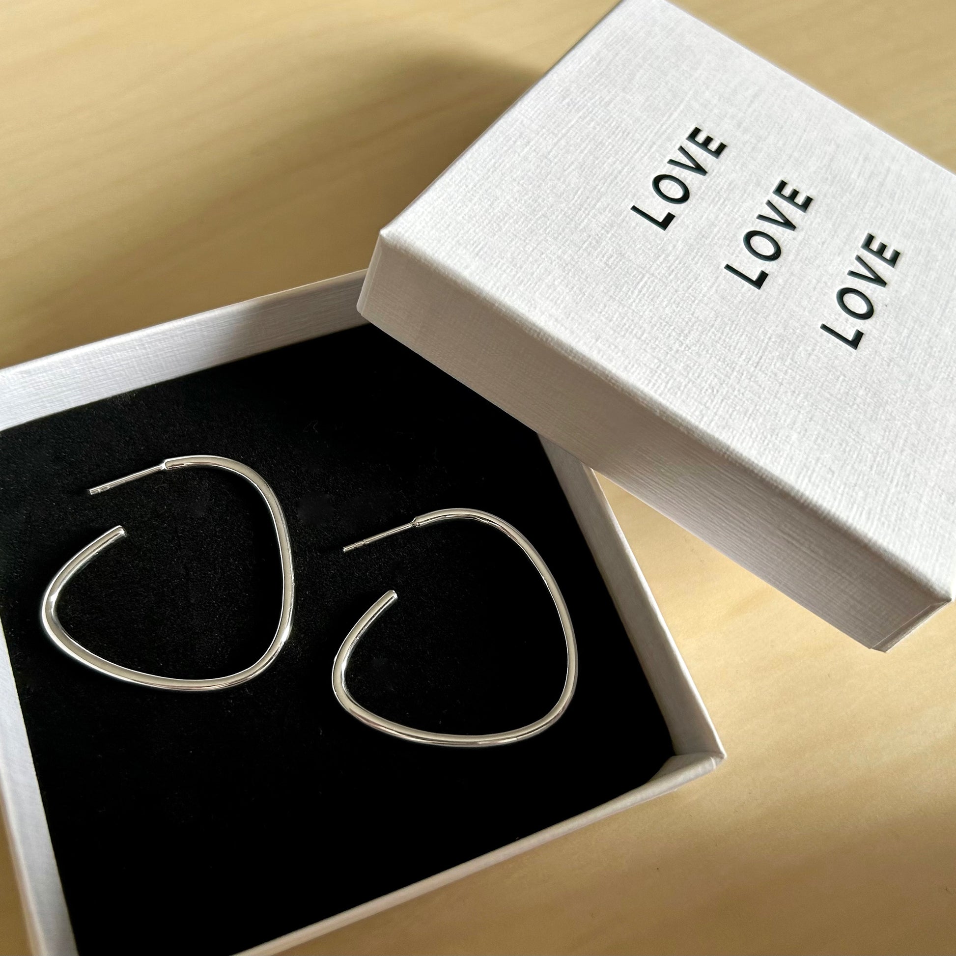 Silver hoop earrings in a 'LOVE' branded box on a beige surface