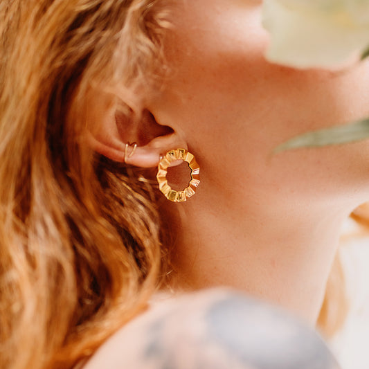 A pair of gold-colored modern geometric earrings with a faceted, circular design
