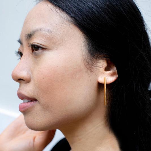 Person wearing gold tubular line earrings.
