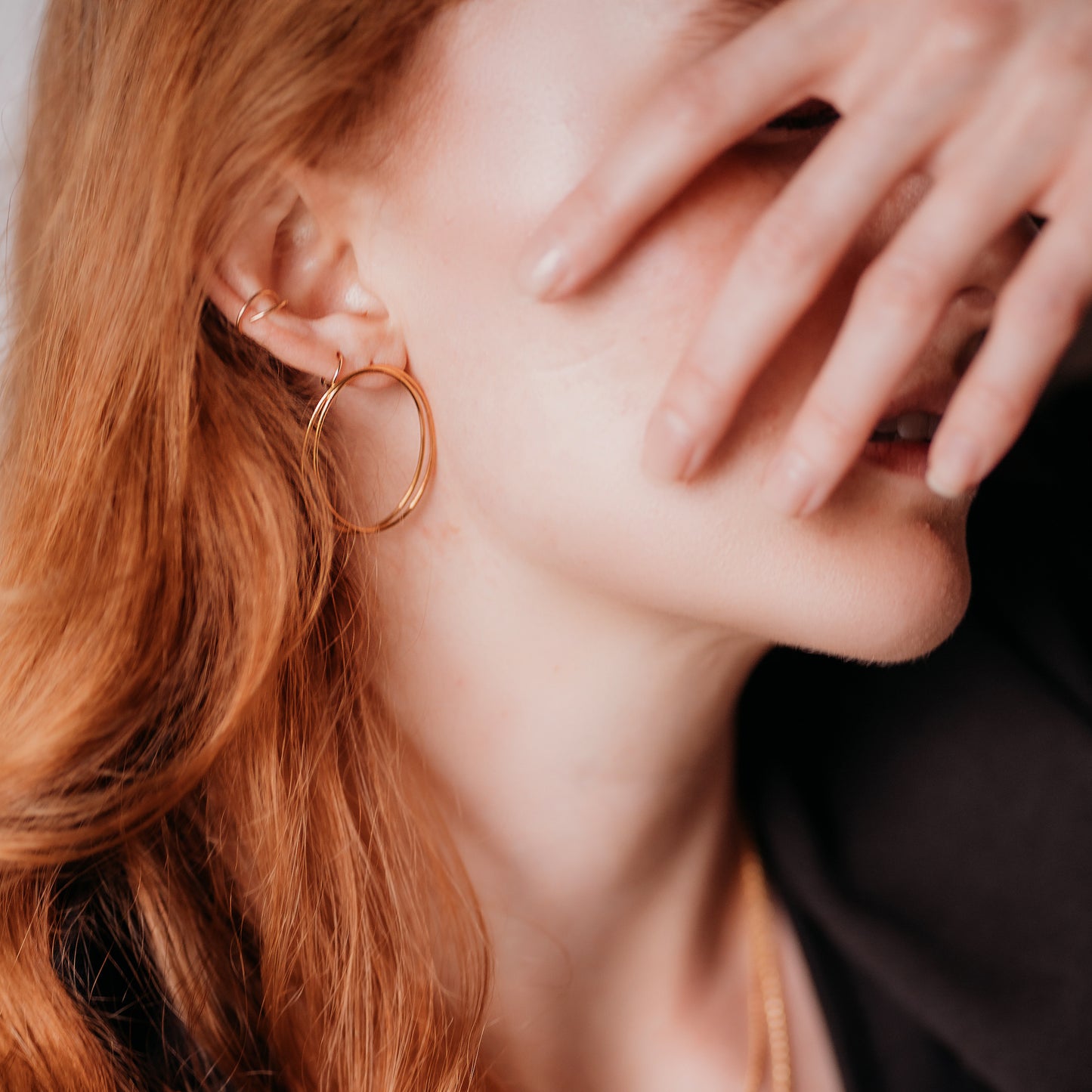 Person wearing circular gold earrings with a hand covering their face.